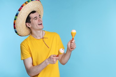 Young man in Mexican sombrero hat with maracas on light blue background. Space for text