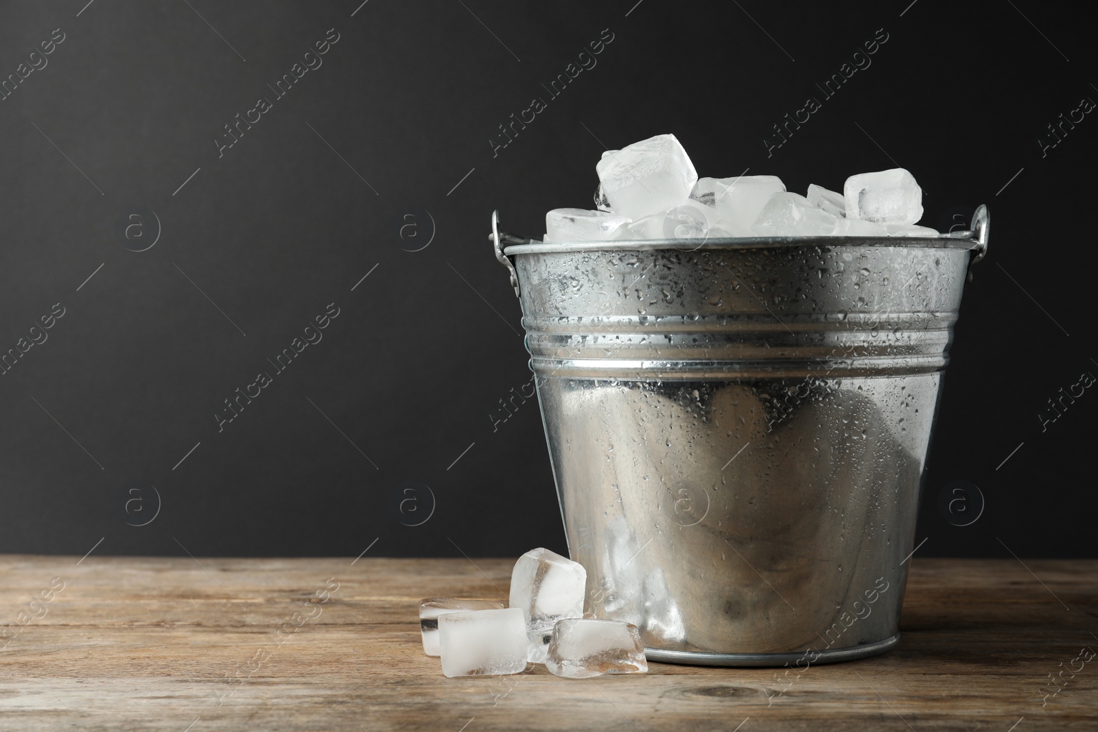 Photo of Metal bucket with ice cubes on wooden table. Space for text