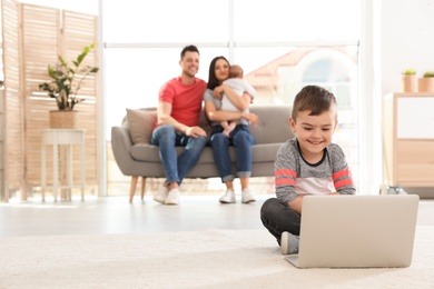 Boy with laptop sitting on floor near his family at home