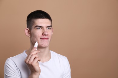 Young man with acne problem applying cosmetic product onto his skin on beige background. Space for text