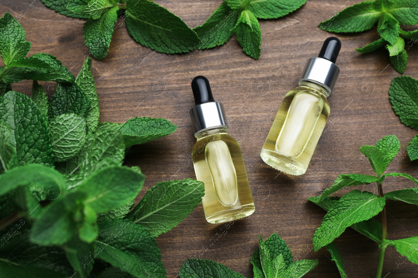 Photo of Bottles of essential oil and mint on wooden table, flat lay