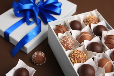 Photo of Box with delicious chocolate candies on brown background, closeup