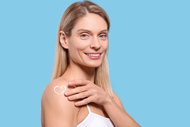 Woman with body cream onto her arm against light blue background, space for text