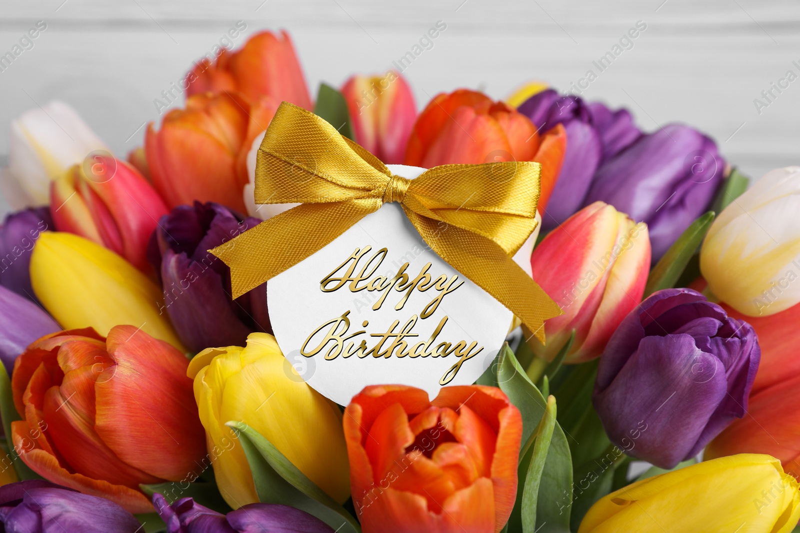 Image of Beautiful bouquet of tulip flowers with Happy Birthday card on light background, closeup