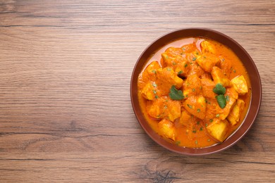 Bowl of delicious chicken curry on wooden table, top view. Space for text