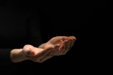 Religion. Woman with open palms praying on black background, closeup. Space for text