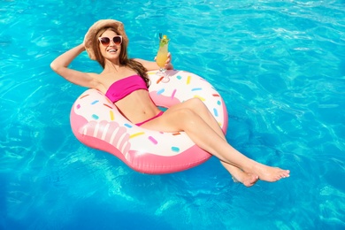 Photo of Young woman with cocktail in pool on sunny day