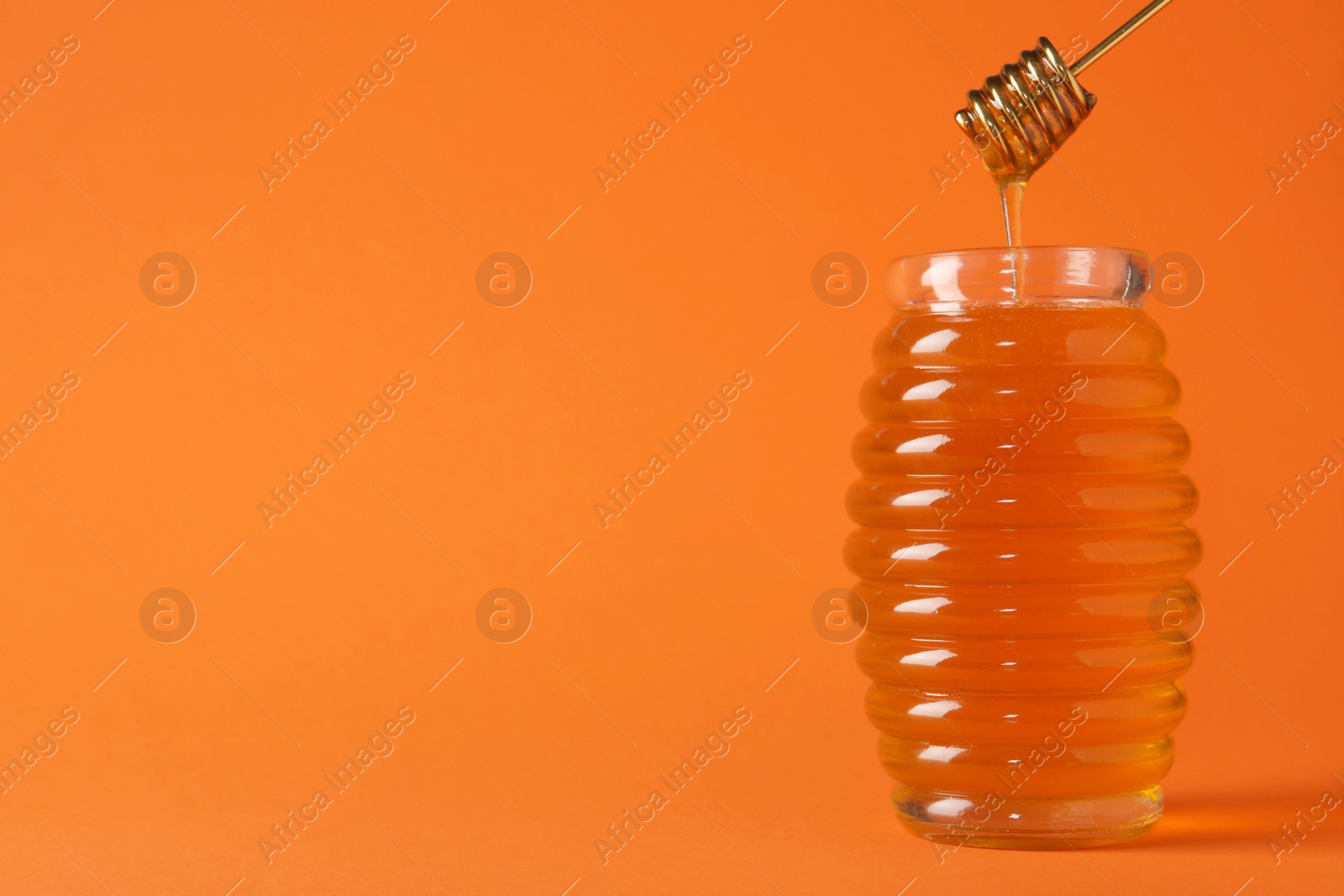 Photo of Jar of organic honey and dipper on orange background. Space for text