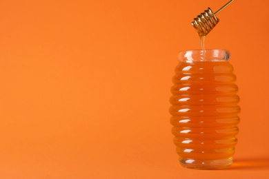 Photo of Jar of organic honey and dipper on orange background. Space for text