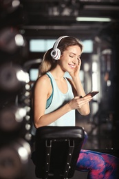 Young woman with headphones listening to music on mobile device at gym