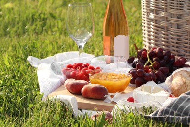 Photo of Picnic blanket with tasty food and cider on green grass outdoors