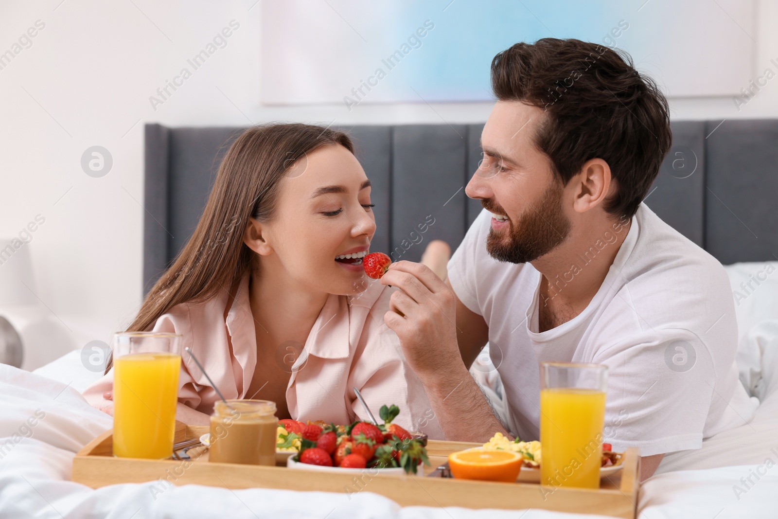 Photo of Tasty breakfast. Happy husband feeding his wife on bed at home