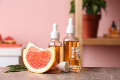 Bottles of essential oil and grapefruit slices on table against blurred background