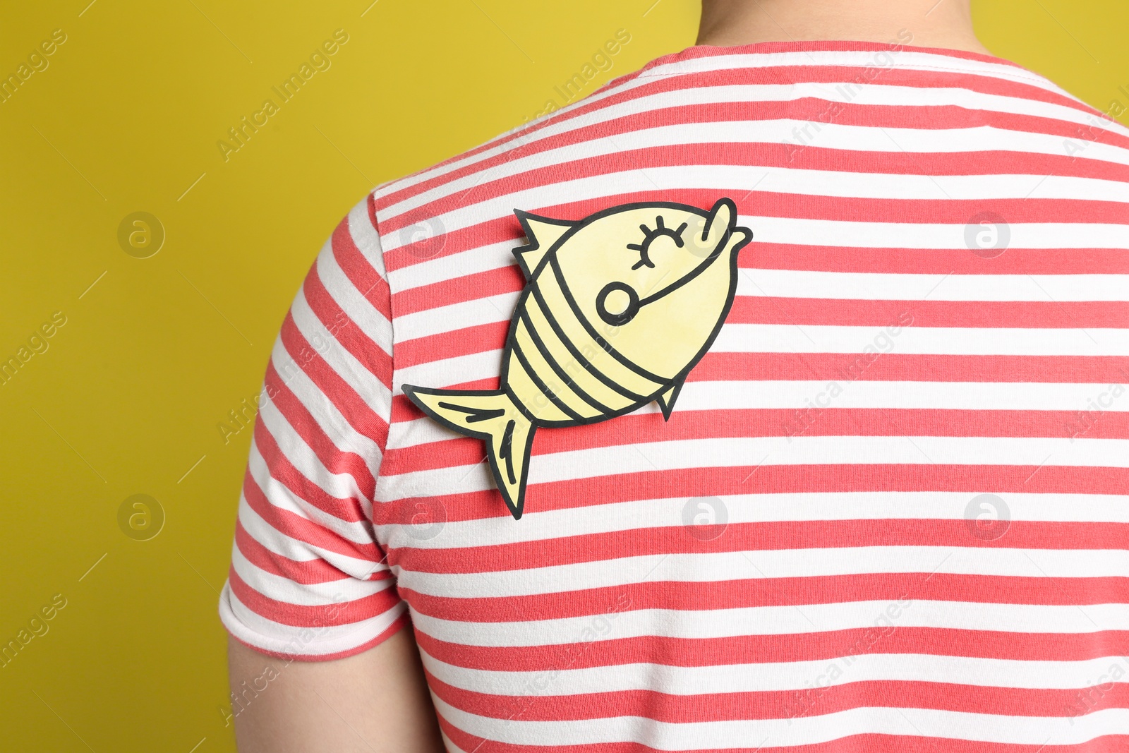 Photo of Man with paper fish sticker on back against yellow background, closeup. April fool's day