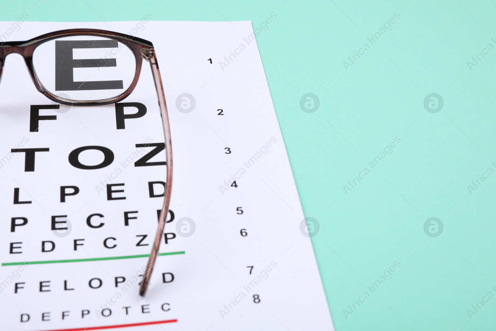 Photo of Vision test chart and glasses on turquoise background, closeup. Space for text