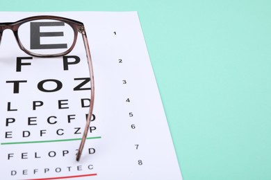 Photo of Vision test chart and glasses on turquoise background, closeup. Space for text