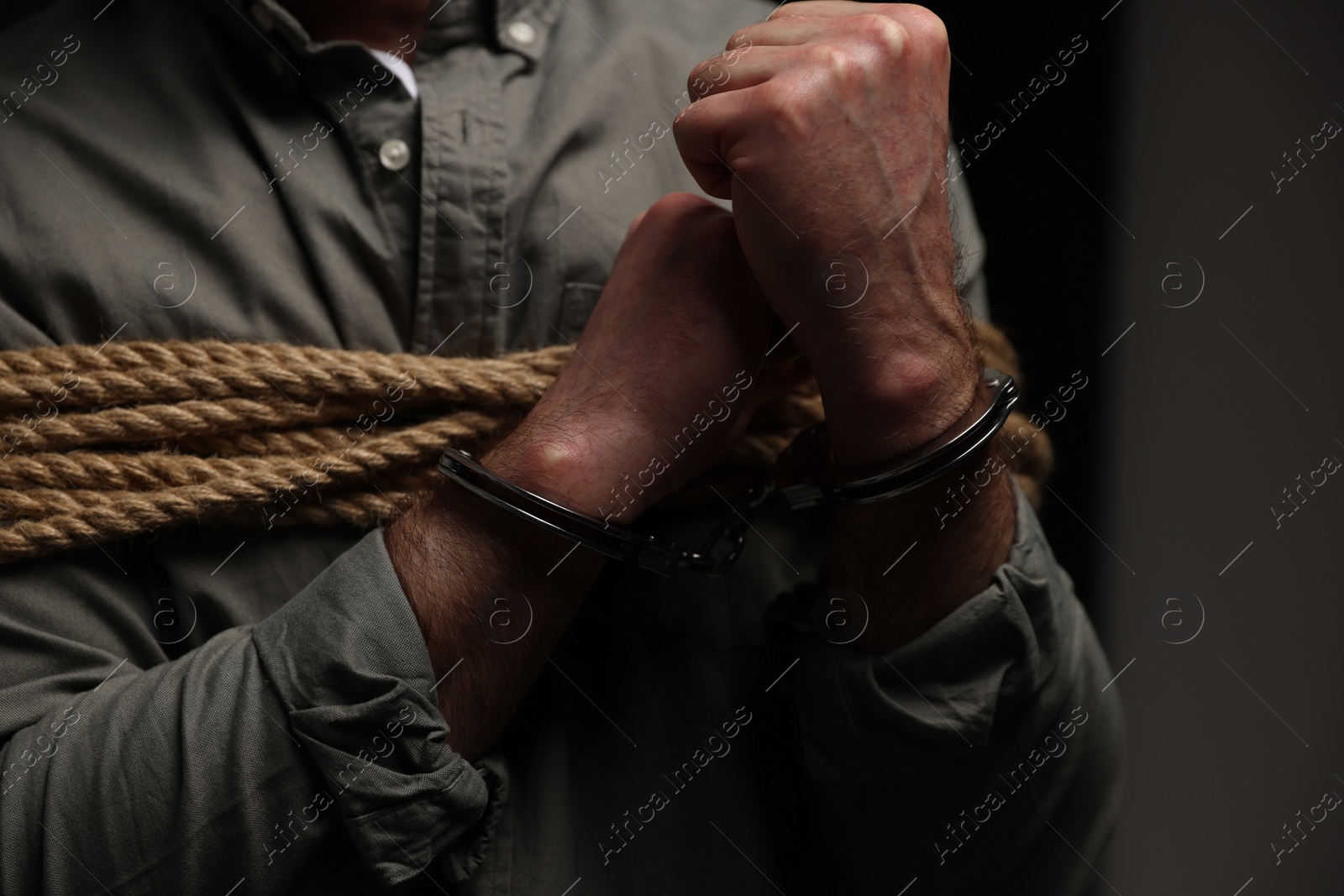Photo of Handcuffed victim tied with rope on dark background, closeup. Hostage taking