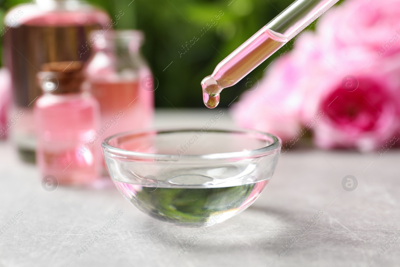 Photo of Dripping rose essential oil into bowl on table