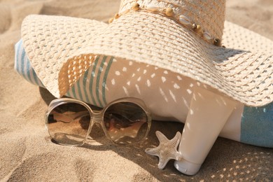 Straw hat, towel, sunscreen, starfish and sunglasses on sand, closeup