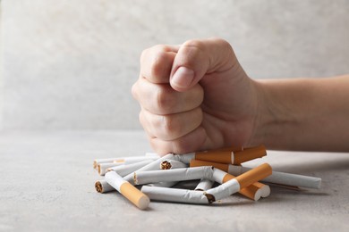 Stop smoking. Woman crushing cigarettes at grey table, closeup. Space for text