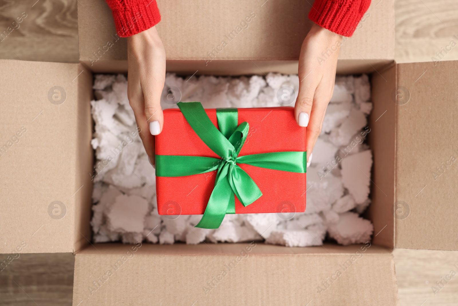 Photo of Woman putting Christmas gift box into parcel at wooden table, top view. Sending present by mail