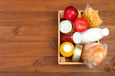 Photo of Humanitarian aid. Different food products for donation in crate on wooden table, top view. Space for text