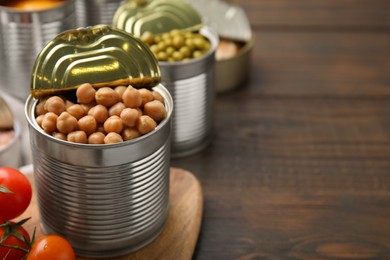 Open tin can with chickpeas and tomatoes on wooden table, closeup. Space for text