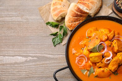 Photo of Delicious chicken curry in pan on wooden table, flat lay. Space for text