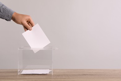 Photo of Man putting his vote into ballot box on light grey background, closeup. Space for text