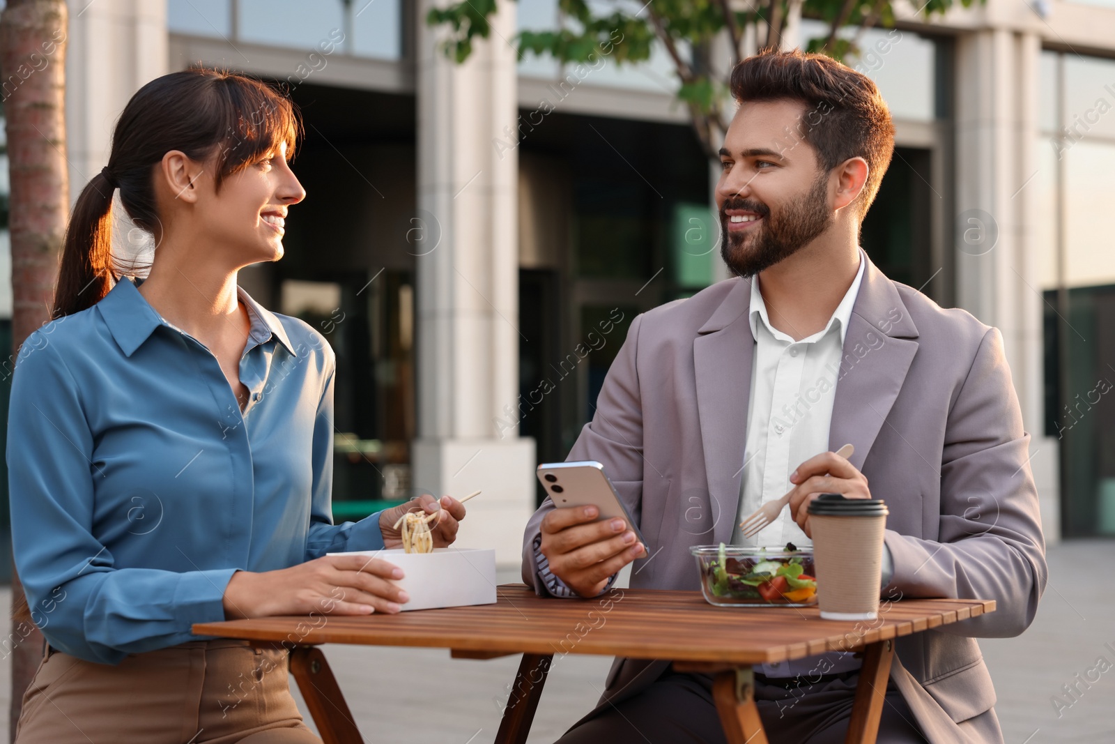 Photo of Happy colleagues having business lunch together at wooden table outdoors