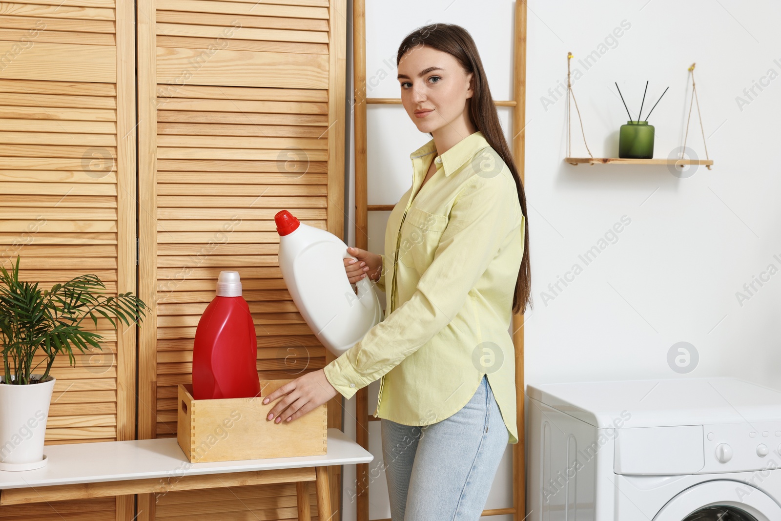 Photo of Beautiful young woman with detergent in laundry room