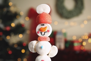 Funny snowman made of marshmallows against blurred Christmas tree, closeup