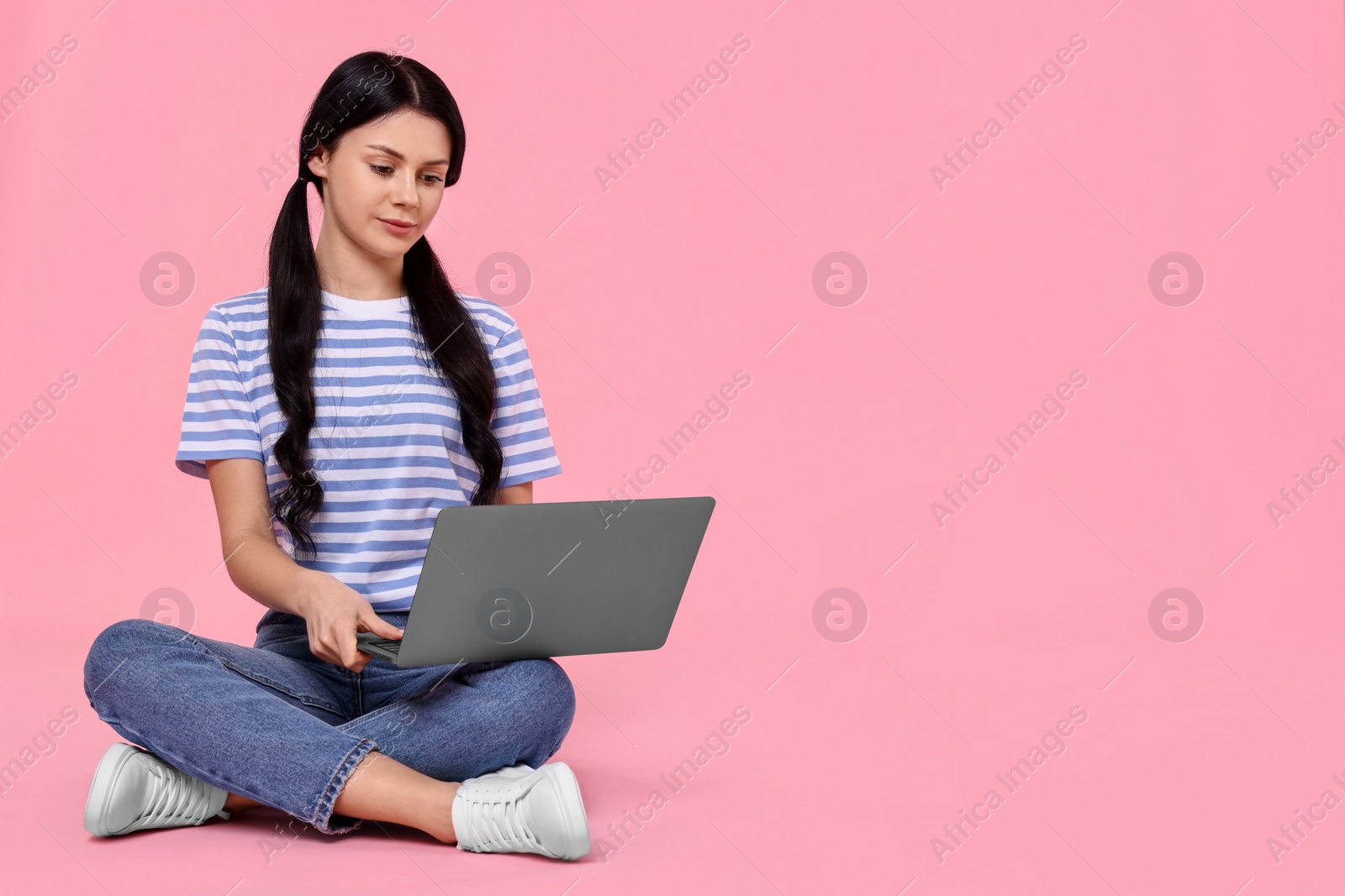 Photo of Student with laptop sitting on pink background. Space for text