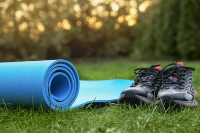 Blue karemat or fitness mat and sneakers on green grass outdoors