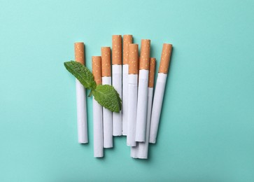 Menthol cigarettes and mint on turquoise background, flat lay