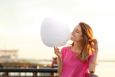 Happy young woman eating cotton candy on waterfront