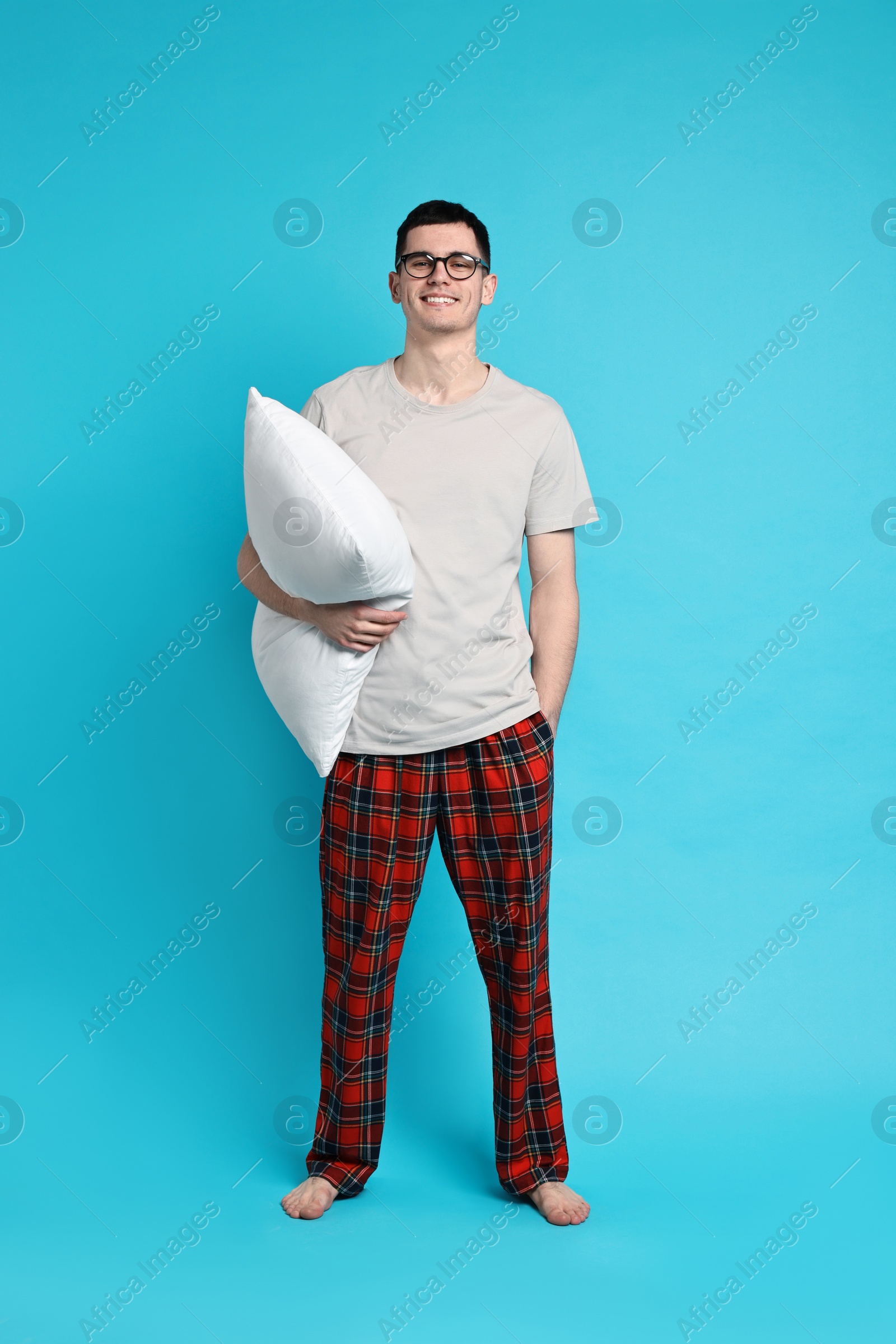 Photo of Happy man in pyjama holding pillow on light blue background