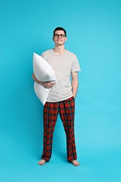 Happy man in pyjama holding pillow on light blue background