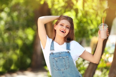 Photo of Young woman with cup of delicious milk shake outdoors