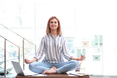 Beautiful woman meditating on table in office during break. Zen yoga