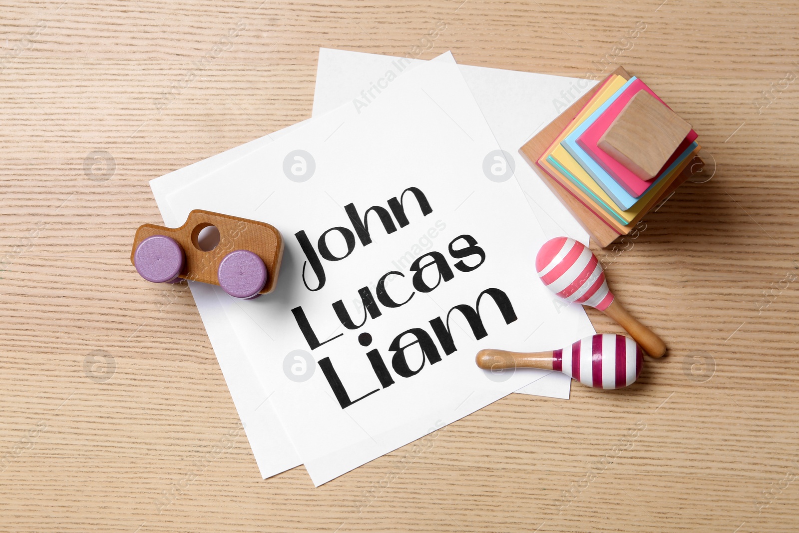 Photo of Paper sheet with written baby names and toys on wooden table, flat lay