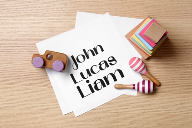 Paper sheet with written baby names and toys on wooden table, flat lay