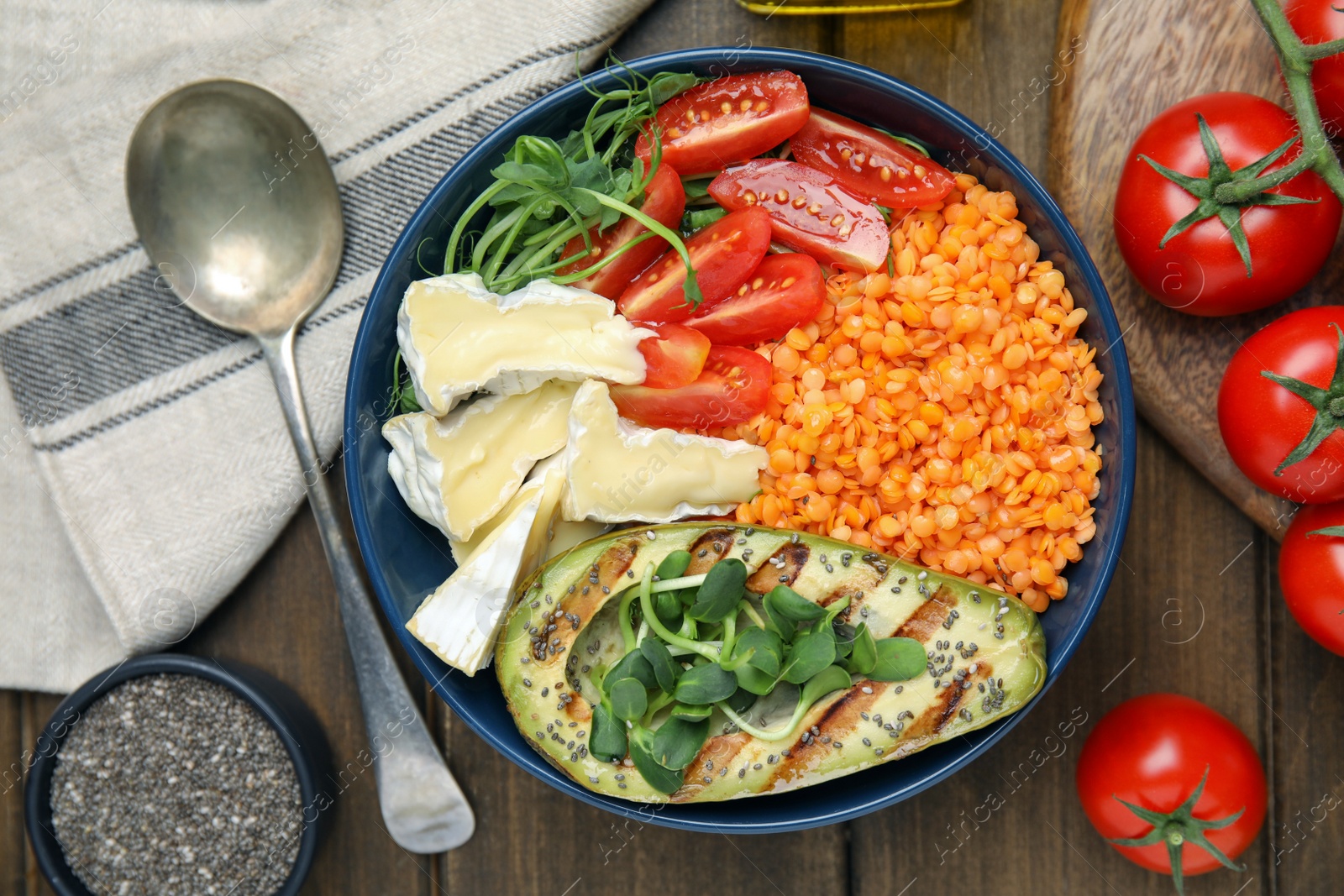 Photo of Delicious lentil bowl with soft cheese, avocado and tomatoes on wooden table, flat lay