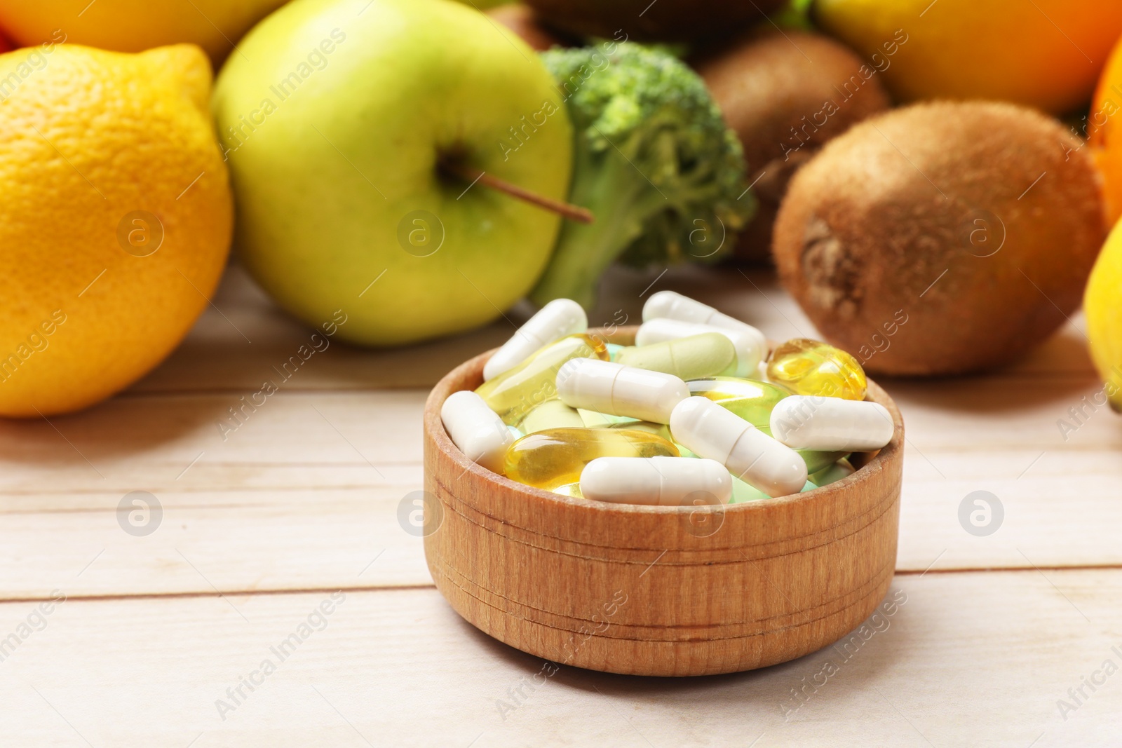 Photo of Dietary supplements. Bowl with different pills near food products on light wooden table, closeup