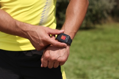 Man with smart watch checking heart rate in health monitor app outdoors, closeup