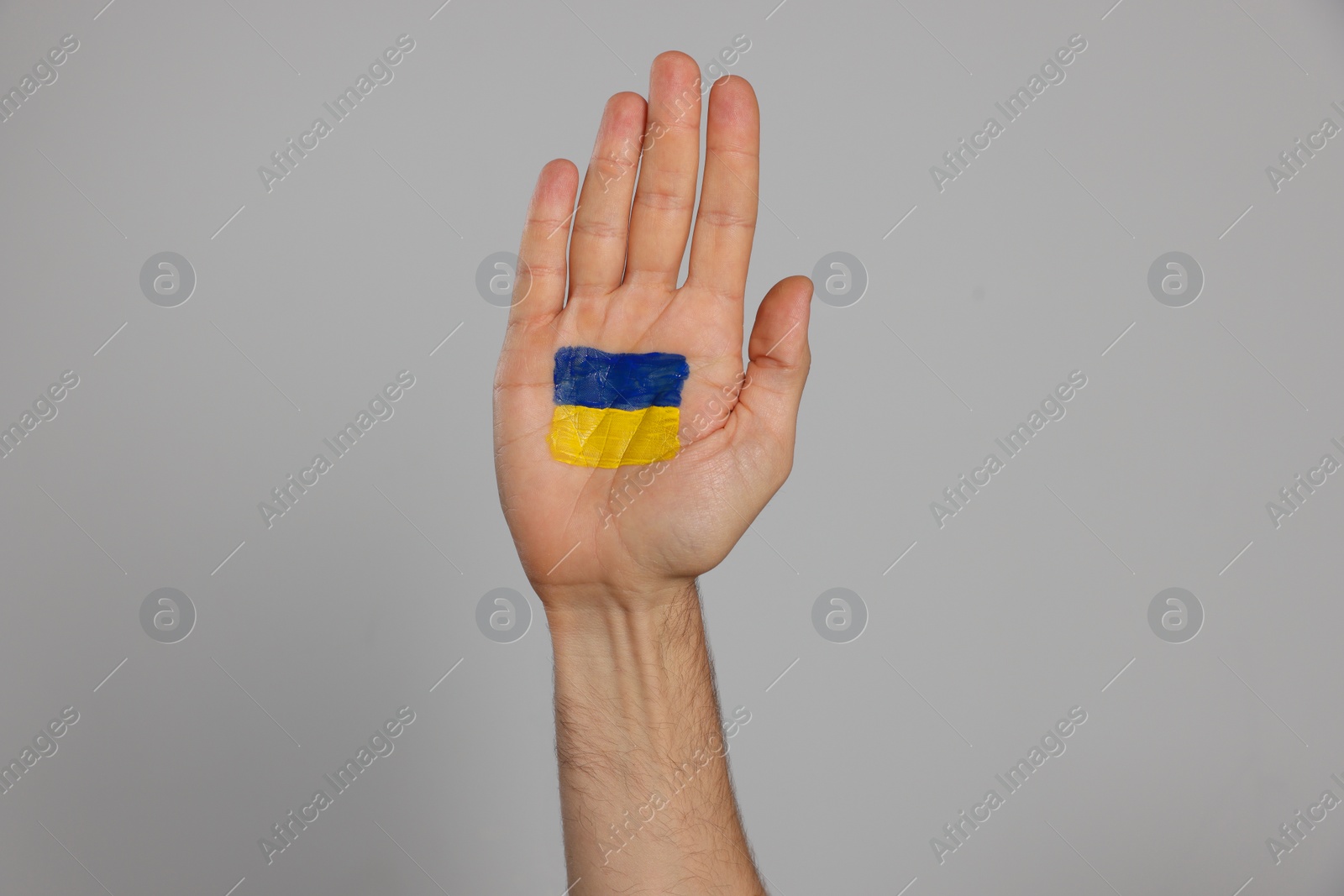 Photo of Man with drawing of Ukrainian flag on palm against light grey background, closeup