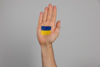Photo of Man with drawing of Ukrainian flag on palm against light grey background, closeup