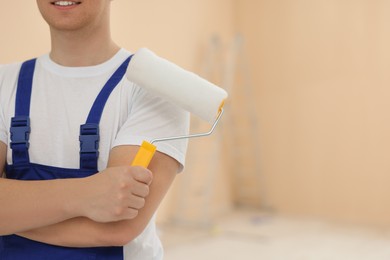 Photo of Worker holding paint roller in unfinished room, closeup. Space for text