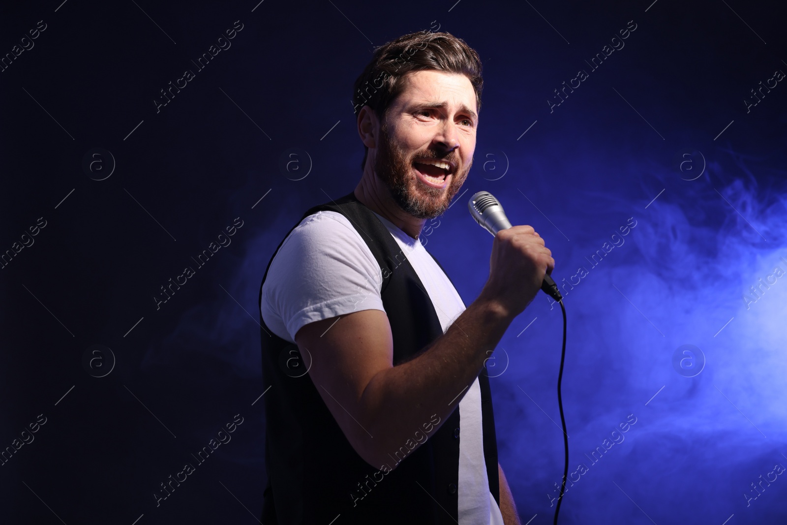 Photo of Handsome man with microphone singing on dark blue background