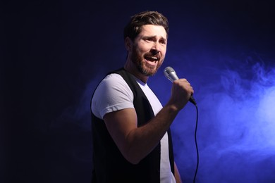 Handsome man with microphone singing on dark blue background